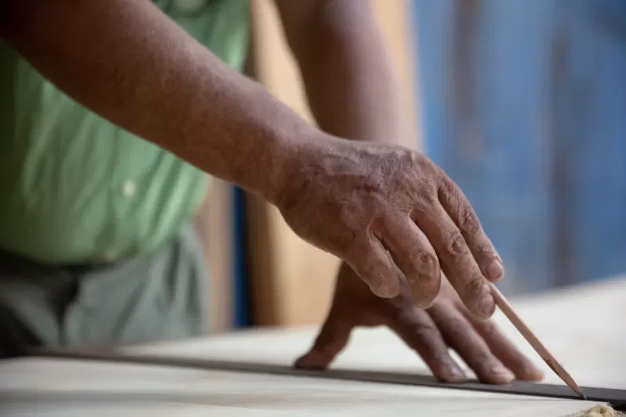 A craftsman's hand marking a measurement on a board with a pencil